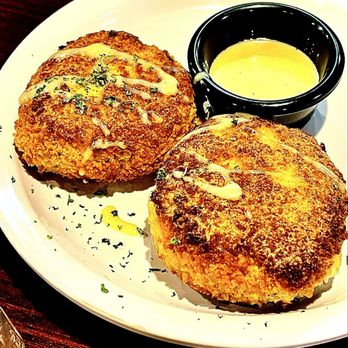 Two golden crab cakes served with dipping sauce